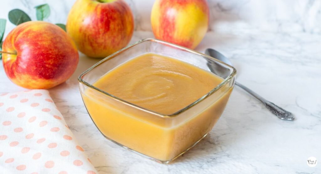A serving of cinnamon applesauce in a white bowl with spoon on the side
