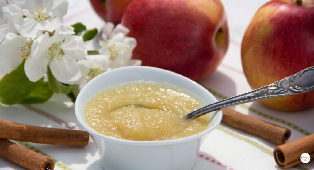 A serving of cinnamon applesauce in a white bowl with spoon on the side