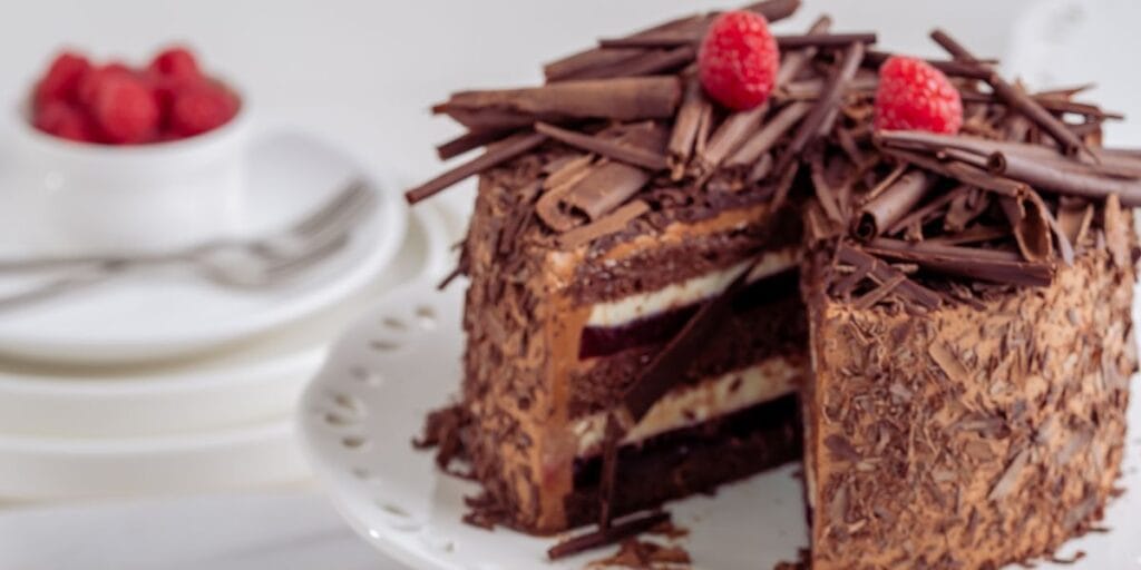 A slice of triple chocolate cake on a plate, showcasing the layers of chocolate cake, frosting, and a decadent chocolate glaze