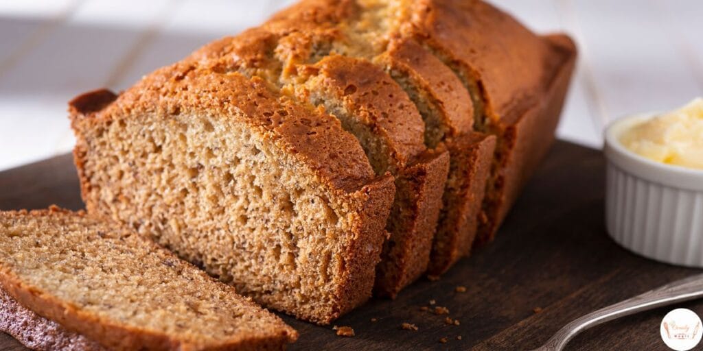 Freshly baked banana bread loaf on a wooden board with a few banana slices around.
