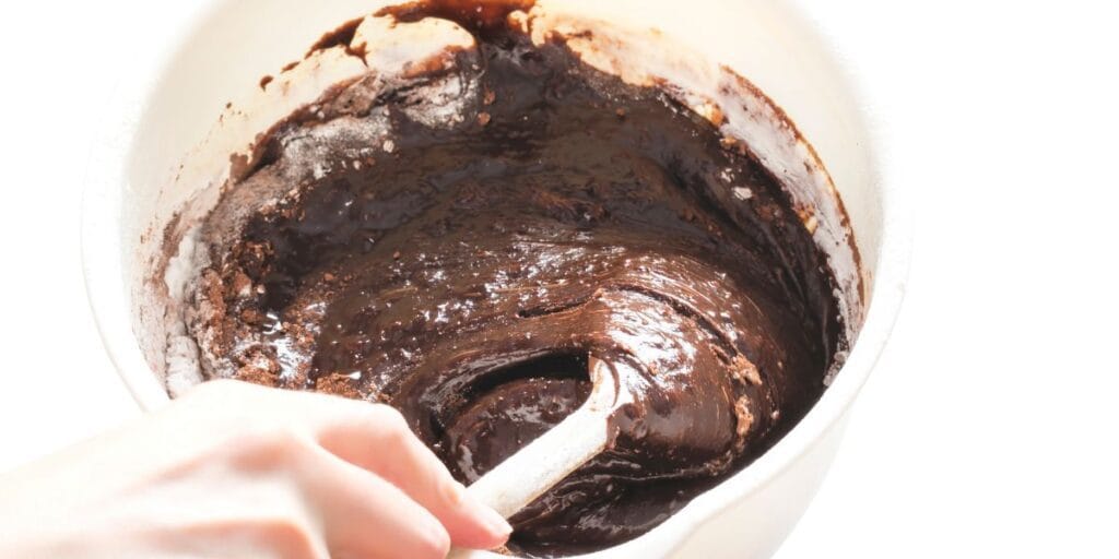 Mixing rich and creamy triple chocolate cake batter in a glass bowl using a spatula