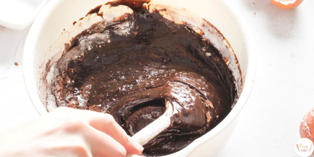 Mixing rich chocolate cake batter in a large bowl with a whisk, showing smooth and creamy texture