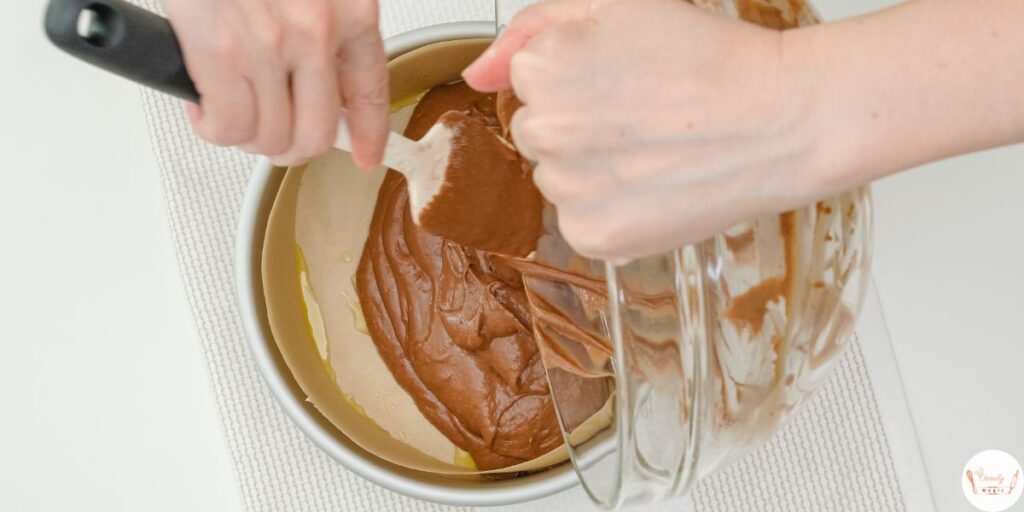 Pouring moist chocolate cake batter into round 8-inch cake pans lined with parchment paper.