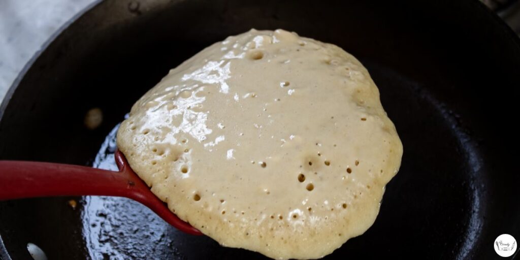 Pancake cooking on griddle with bubbles on top