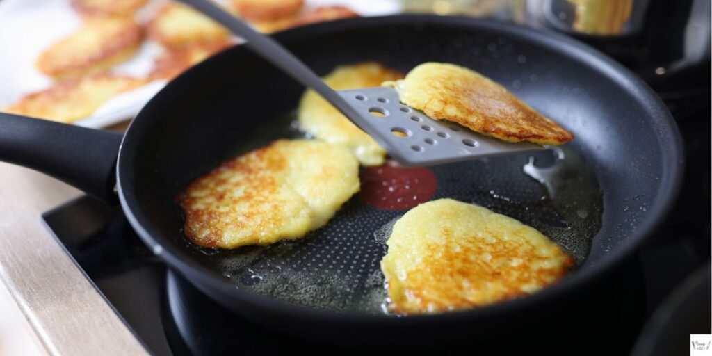 Potato pancakes frying in a pan, turning golden brown with crisp edges."