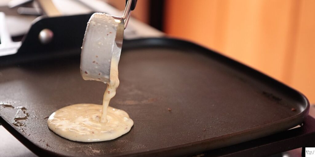 Scooping potato pancake batter into a hot skillet with sizzling butter and oil.