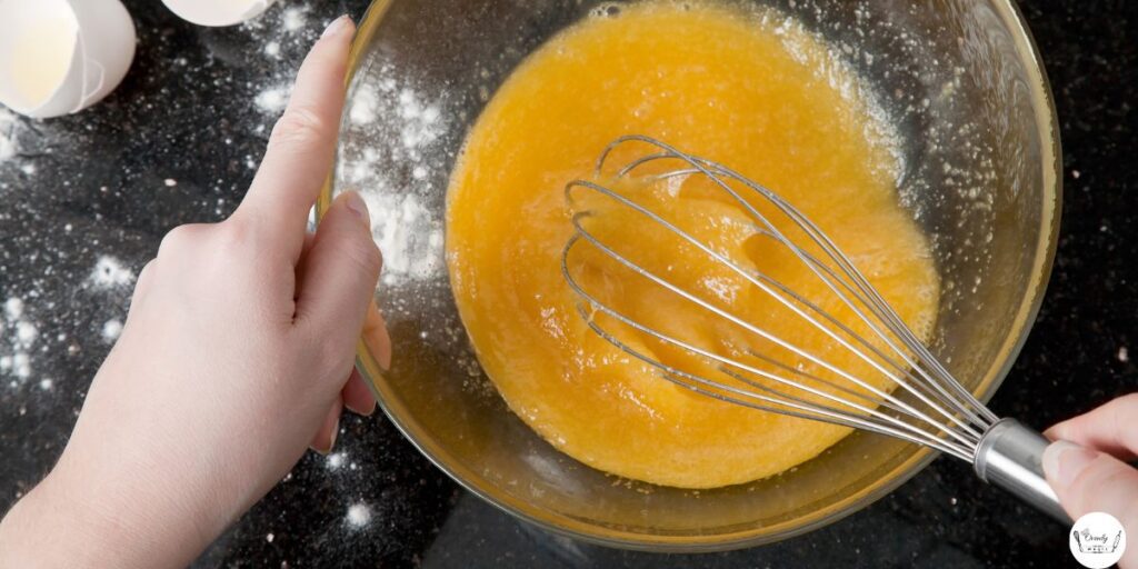 Sugar, eggs, and oil being whisked together in a glass bowl.