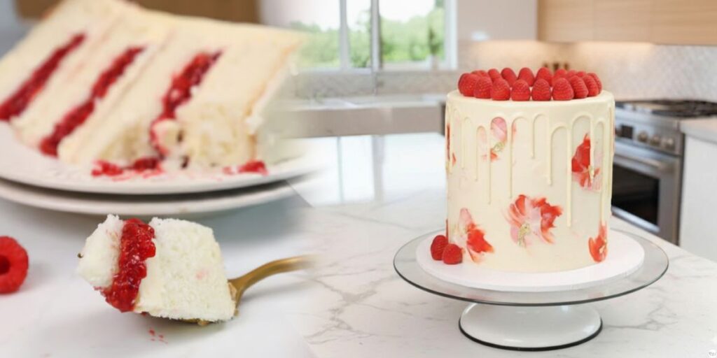 White Chocolate Raspberry Cake on a stand with pink frosting and fresh raspberries