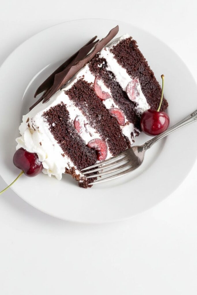 Slice of moist Black Forest Cake showing chocolate layers, cherries, and creamy frosting