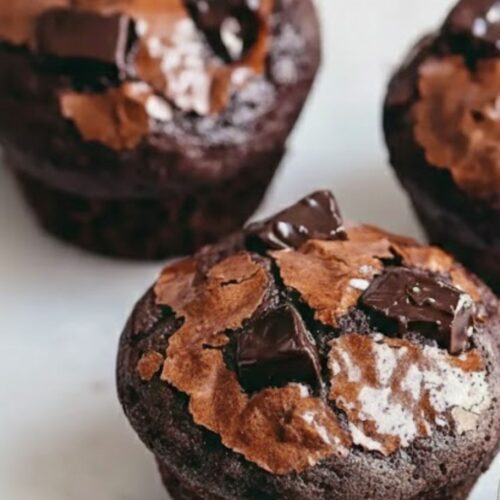 Freshly baked Brownie Muffins on a plate or tray, dark chocolatey tops, some with a gooey interior visible.