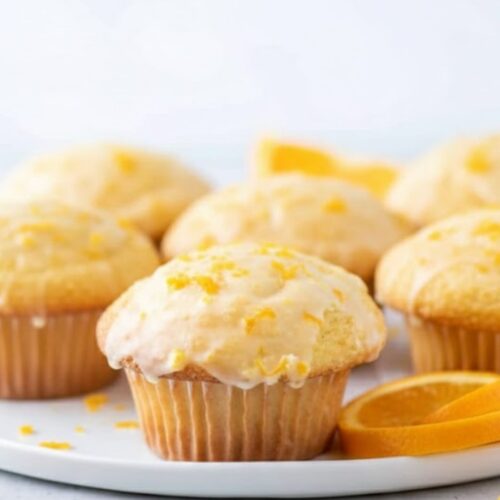 Freshly baked Orange Muffins on a plate or wooden board, golden brown with orange zest sprinkled on top.