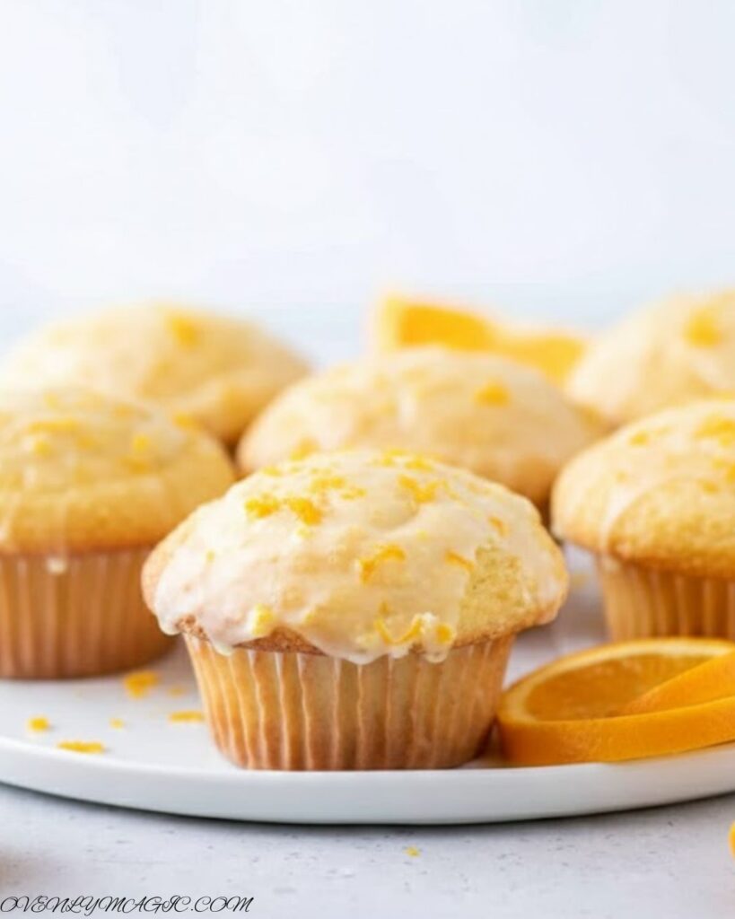 Freshly baked Orange Muffins on a plate or wooden board, golden brown with orange zest sprinkled on top.