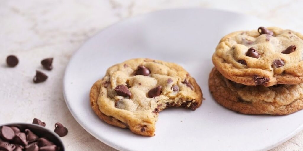 Freshly baked chocolate chip cookies with golden edges, chewy centers, and melted chocolate chips, stacked on a cooling rack.