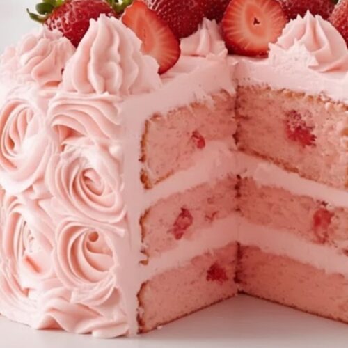 Strawberry Cake with Strawberry Frosting on a white plate, topped with fresh strawberries, soft and moist pink layers visible