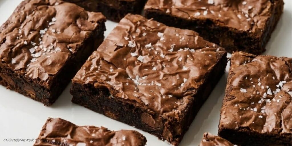 Fudgy Malted Brownies with brown butter, malted milk powder, melty chocolate chips, and shiny crinkly top, served in squares on a parchment-lined pan.